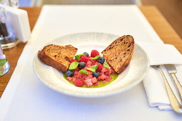 Tuna tartare with raspberries and blueberries in a white plate.