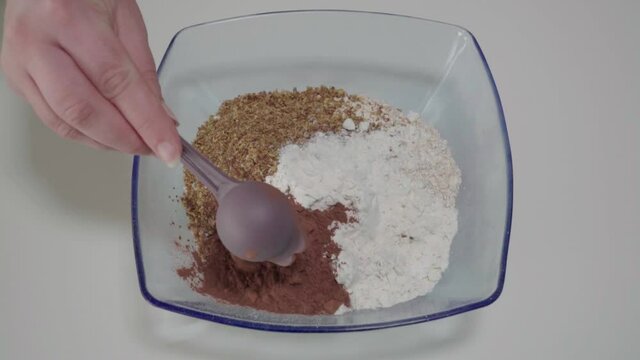 Adding tablespoon of cocoa powder to dry ingredients in mixing bowl, Overhead