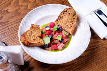 Tuna tartare with raspberries and blueberries in a white plate.