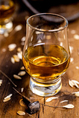 Small tasting glasses with aged Scotch whisky on old dark wooden vintage table with barley grains