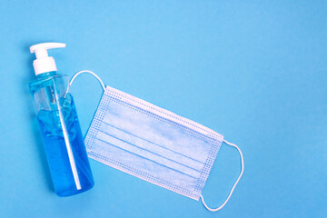Flat lay bottle of sanitizing gel and surgical mask on blue background, health care concept