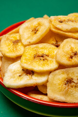 Healthy snack, crispy dehydrated unsugared banana chips in bowl on green background