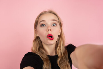 Funny selfie. Portrait of young emotional woman gesturing isolated on pink studio background. Human emotions, facial expression, sales, ad concept. Blonde caucasian pretty model gesturing. Copyspace.