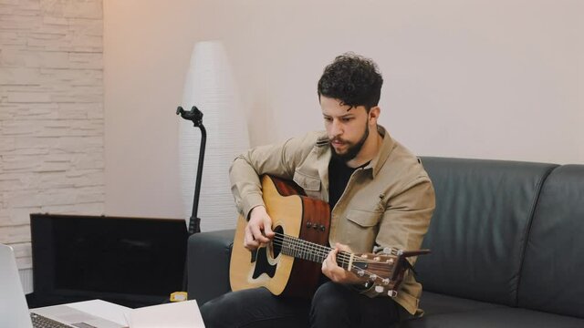 chico feliz joven tocando la guitarra dando clases de guitarra mientras esta sentado en salon luminoso en un moderno apartamento