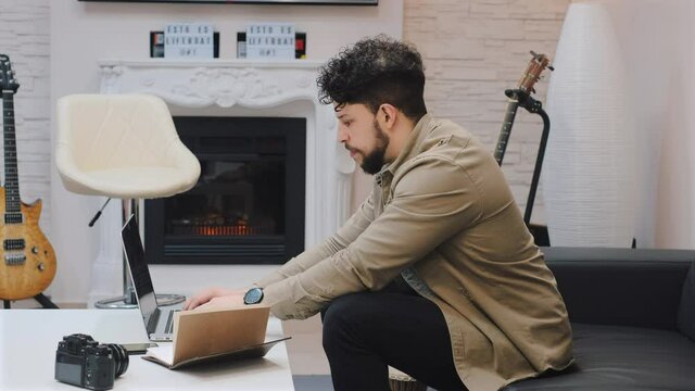 chico feliz joven escribiendo en el portatil mientras esta sentado en salon luminoso en un moderno apartamento