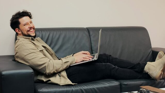 chico feliz joven escribiendo en el portatil mientras esta sentado en salon luminoso en un moderno apartamento