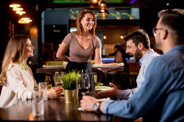 Waiter woman serving group of friends with food in the restaurant