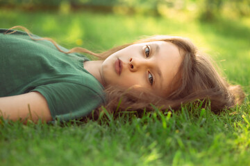 Happy smiling fun casual kid girl lying on the grass on nature summer background. Closeup