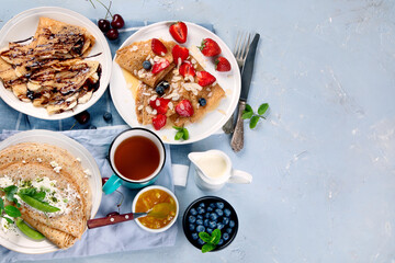 Variety of homemade crepes on grey background.