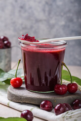Homemade sweet and sour cherry jam with fresh cherries on light table, copy space