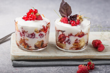 Trifle. Layered trifle dessert with sponge cake, whipped cream and raspberries in serving glasses on light  background. With copy space