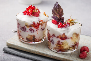 Trifle. Layered trifle dessert with sponge cake, whipped cream and raspberries in serving glasses on light  background. With copy space