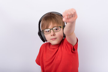 Portrait of boy like superman holding hand with fist up. Child with glasses and headphones, white background