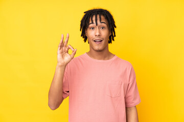 Young african american man isolated on yellow background surprised and showing ok sign