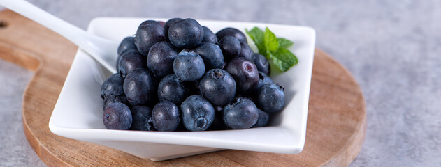 Pile of blueberry fruit in a bowl plate on a tray over gray cement concrete background, close up, healthy eating design concept.