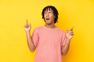 Young african american man isolated on yellow background surprised and pointing up