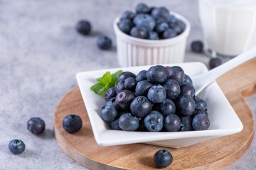 Pile of blueberry fruit in a bowl plate on a tray over gray cement concrete background, close up,...