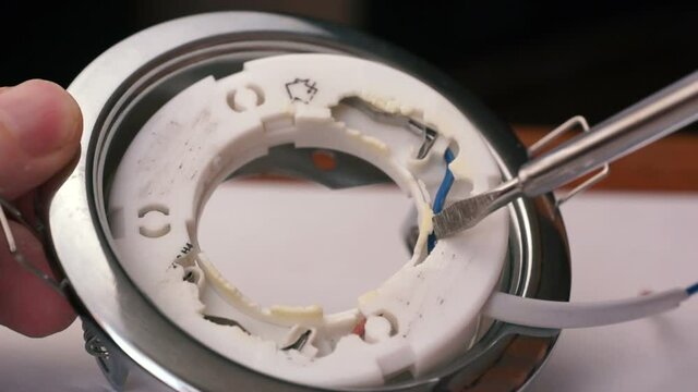 Close-up of a LED broken down lamp dismantled from the ceiling, an electrician using a screwdriver disassembles the lamp, repairing a home electrician. Selective focus, shallow depth of field