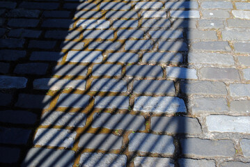 Shadows of Old Iron Railings on Rough Granite Blocks of Roadway 