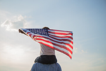 Little boy lets the american flag fly in his hands on the wind at the green field. Patriotic family celebrates usa independence day on 4th of July. Constitution and Patriot Day.