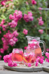 Obraz na płótnie Canvas Fresh Rose lemonade or cokctail with ice and fresh roses over natural garden
