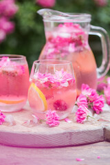 Fototapeta na wymiar Fresh Rose lemonade or cokctail with ice and fresh roses over natural garden