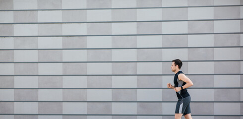 Jogging in city. Slender guy in sportswear with fitness tracker, runs