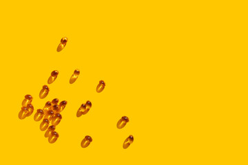 Vitamin D concept in the sunlight. Vitamin gelatin capsules scattered on yellow background