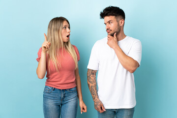 Young caucasian couple isolated on blue background standing and thinking an idea