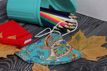 A pencil case in the form of a trash can. It contains colored pencils. Nearby is a notepad and a...