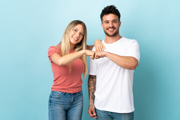 Young caucasian couple isolated on blue background bumping fists