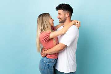 Young caucasian couple isolated on blue background hugging