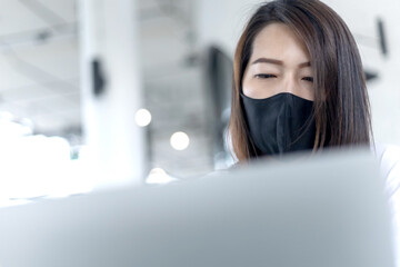 Businesswoman wearing medical facial mask working alone on laptop at cafe after coronavirus...