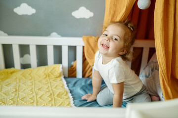 Little cute curly haired girl two years old playing in her canopy bed at home