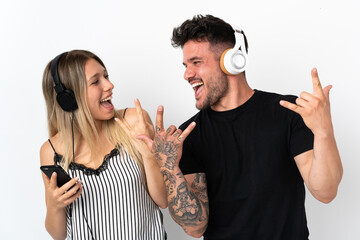 Young caucasian couple on white background listening music making rock gesture
