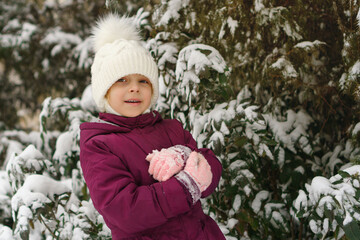 Portrait of a little cute emotional girl on a background of a snowy Christmas tree. Walk on a winter snowy day. Happy childhood. Games, freedom and carefree