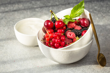 Bowl of fresh berries with Bowl of fresh berries with Labneh middle eastern lebanese cream cheese on grey background. Natural hard light on grey background. Natural hard light