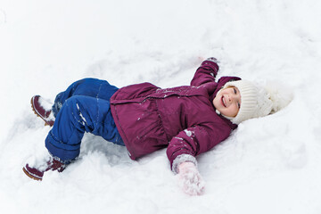 Fototapeta na wymiar Full length portrait of a little playful girl in the snow. She has fun and leads a healthy lifestyle. Walk on a winter snowy day. Happy childhood. Games, freedom and carefree