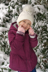 Portrait of a little cute emotional girl on a background of a snowy Christmas tree. Walk on a winter snowy day. Happy childhood. Games, freedom and carefree