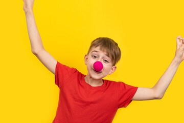 Cheerful clown kid child. April fools day. Child with red clown nose on yellow background.