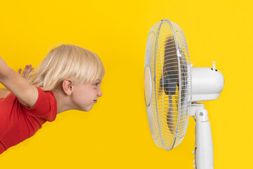 Blond boy with ventilator relaxing on yellow background. Summer heat