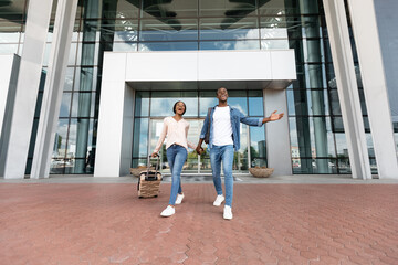 After Arrival. Joyful black couple leaving airport terminal with suitcases