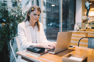 Smart casual Caucasian freelancer using laptop computer for doing distance projecting research informative publication, skilled woman making booking and banking via content application on netbook