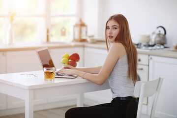 Young woman working in laptop and tablet at home at her kitchen