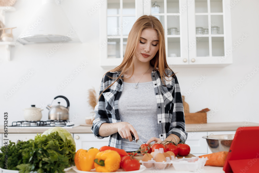 Wall mural young woman cooking at home at kitchen with tablet