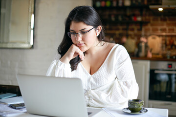 Beautiful serious young woman sales manager with black loose hair and chubby cheeks working...