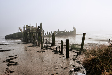 Oare, Faversham, Kent, UK. Derelict boats and jetty at Oare Creek. Low tide and early morning mist.