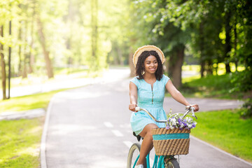 Lovely African American girl cycling on bike in countryside on sunny day, free space