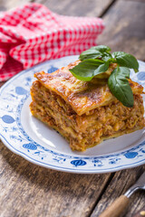 Meat lasagna with fresh basil and parmesan cheese in a plate on wooden table. close up. italian food.