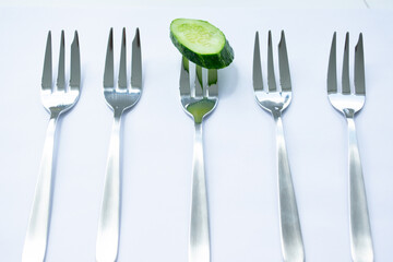 A piece of green cucumber on a fork on white background
